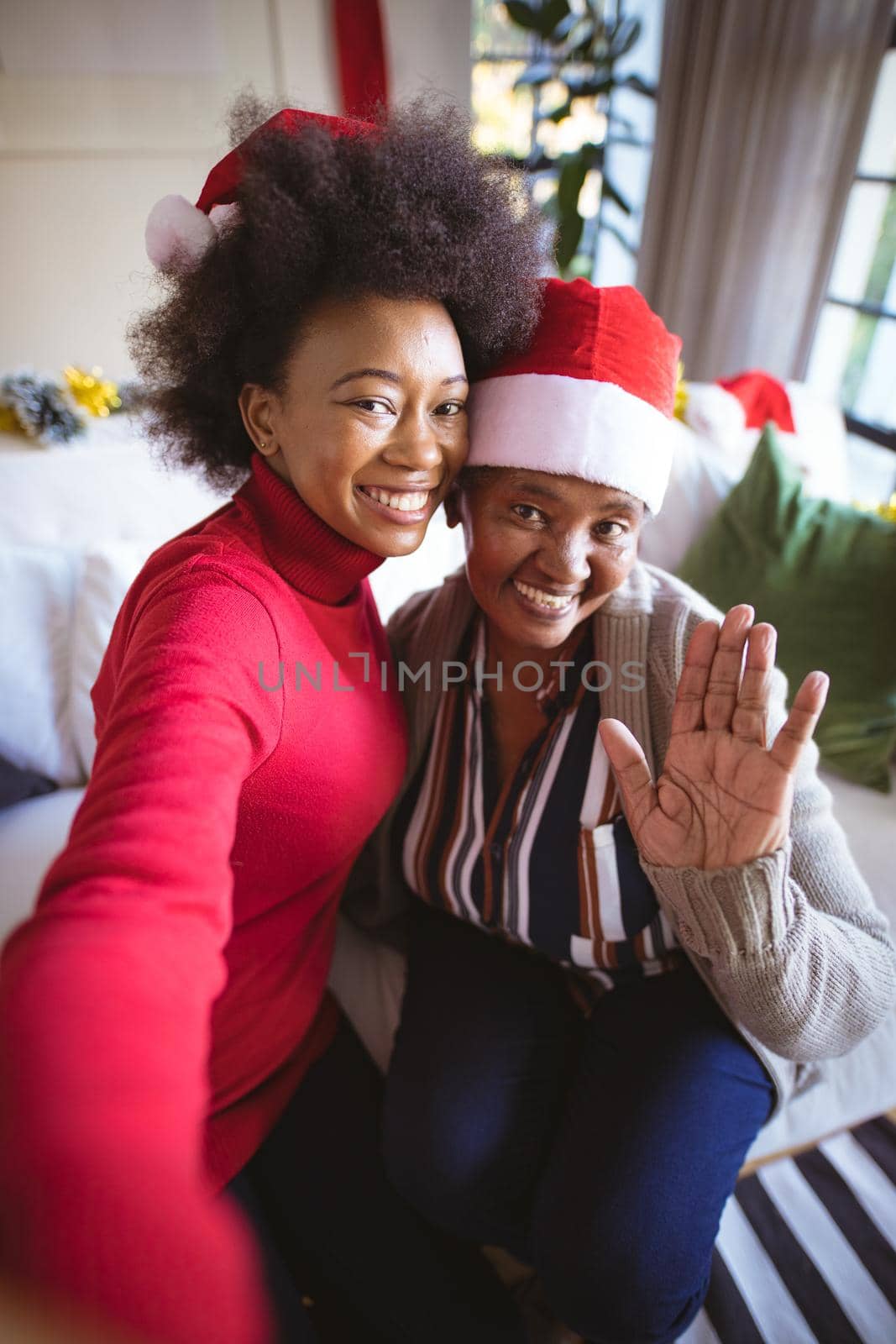 Smiling african american adult daughter and senior mother in santa hats taking christmas selfie by Wavebreakmedia