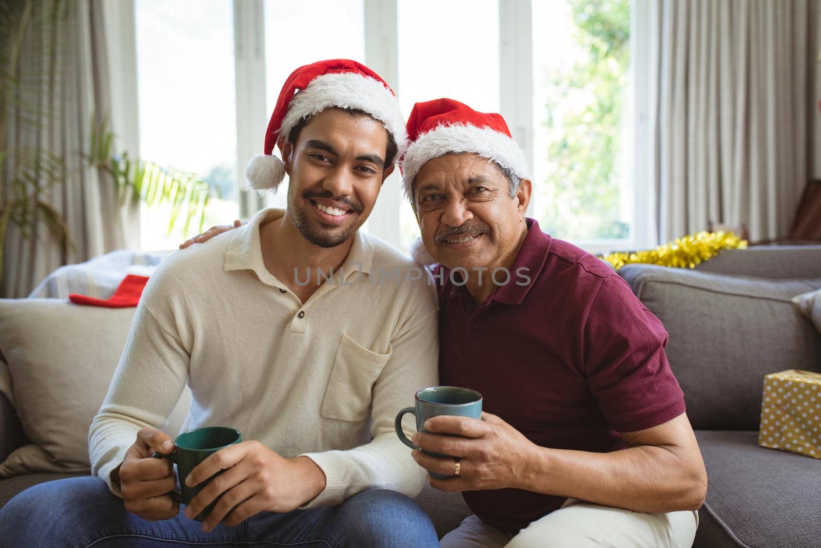 Portrait of happy biracial adult son and senior father in santa hats making christmas video call. christmas, festivity and communication technology.