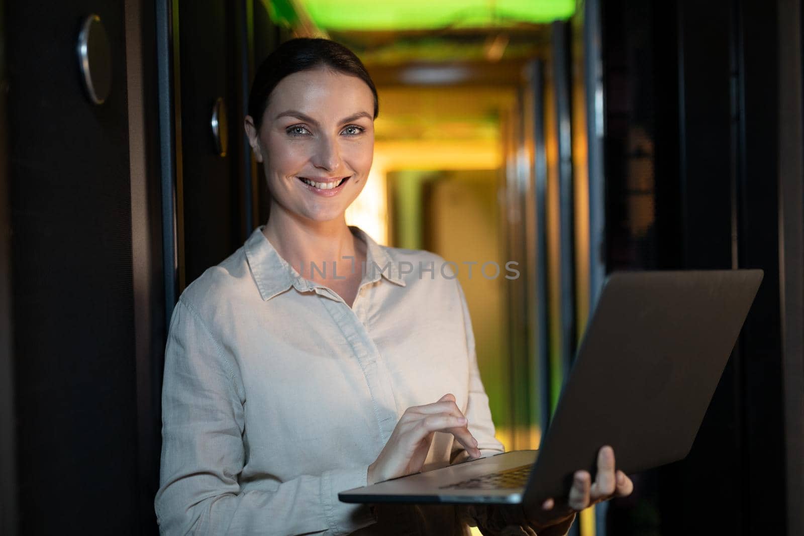 Portrait of caucasian female engineer smiling while using laptop in computer server room. database server management and maintenance concept