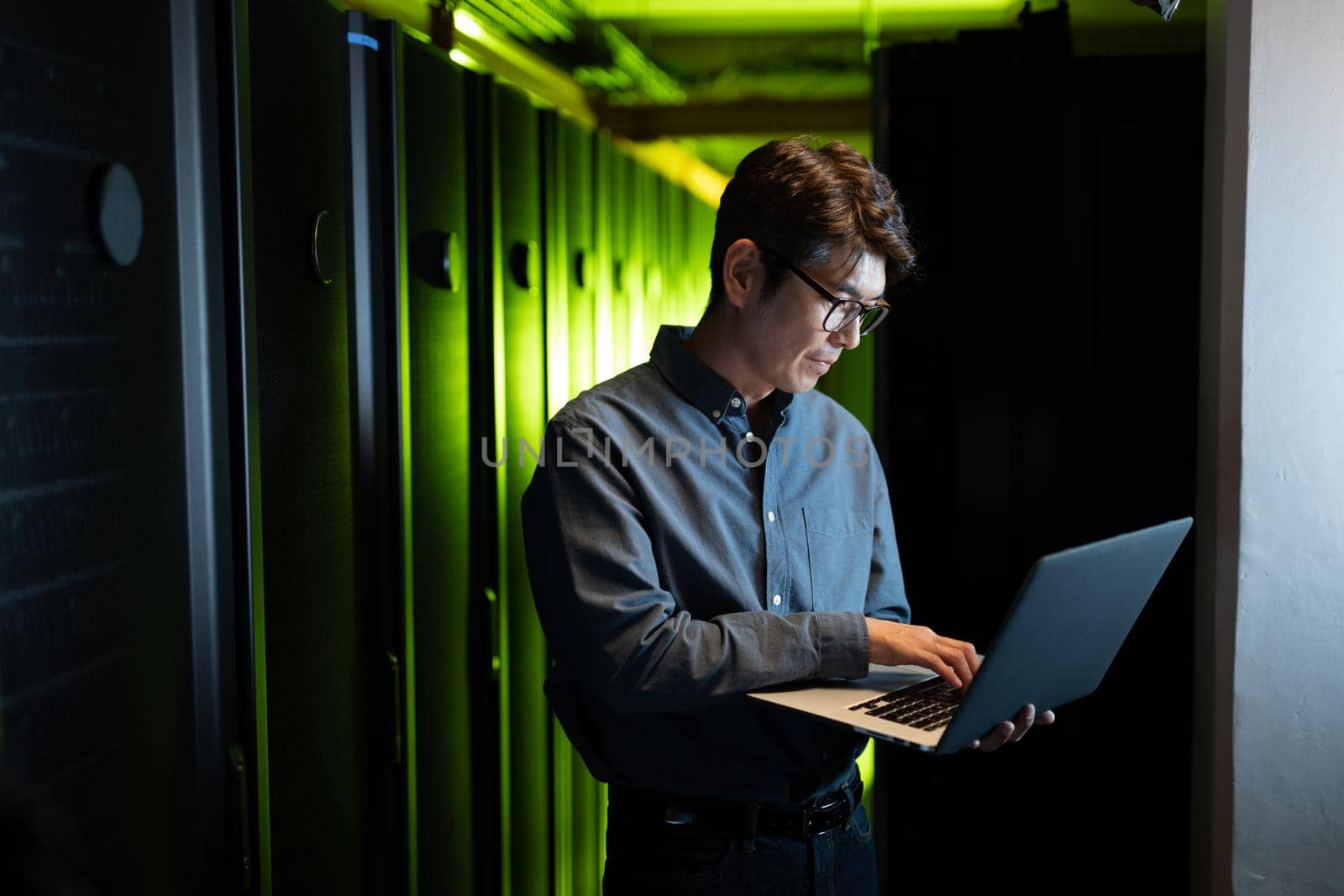 Asian male engineer using laptop in computer server room. database server management and maintenance concept