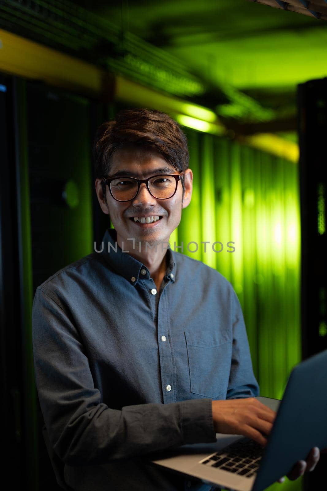 Portrait of asian male engineer smiling while using laptop in computer server room. database server management and maintenance concept