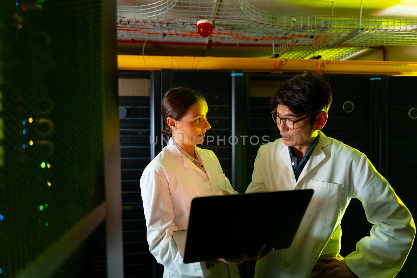 Diverse male and female engineers wearing aprons using laptop while inspecting in server room by Wavebreakmedia