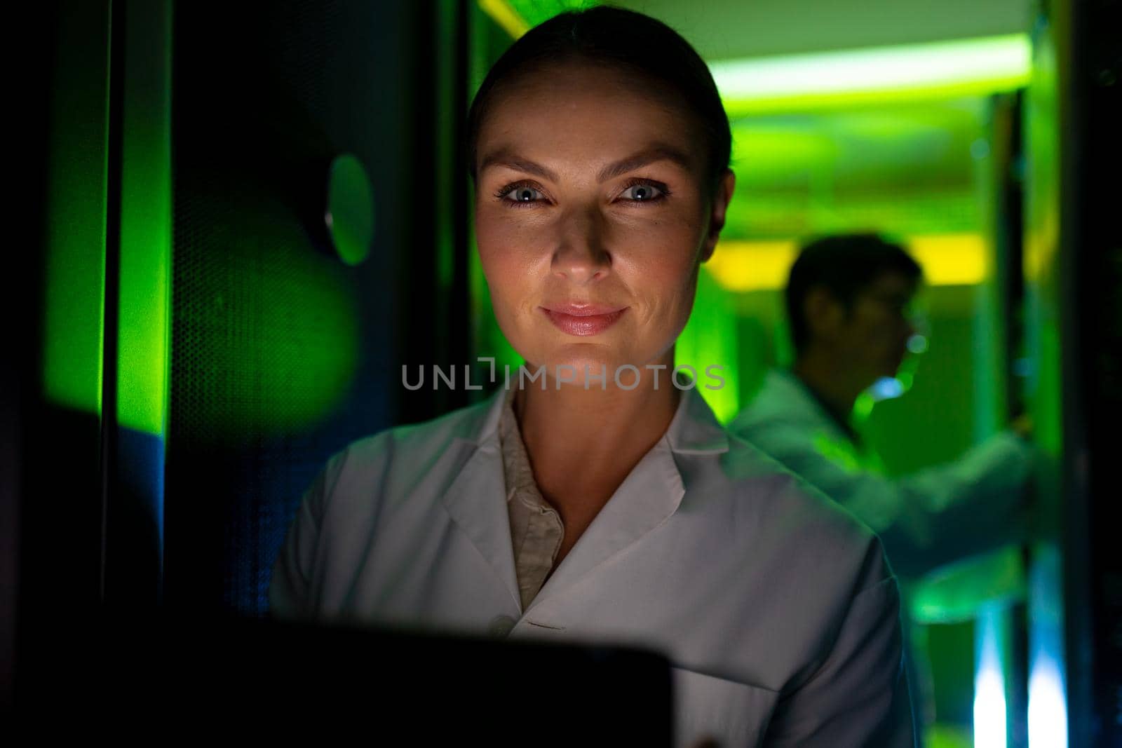 Portrait of caucasian female engineer wearing an apron using laptop in computer server room. database server management and maintenance concept