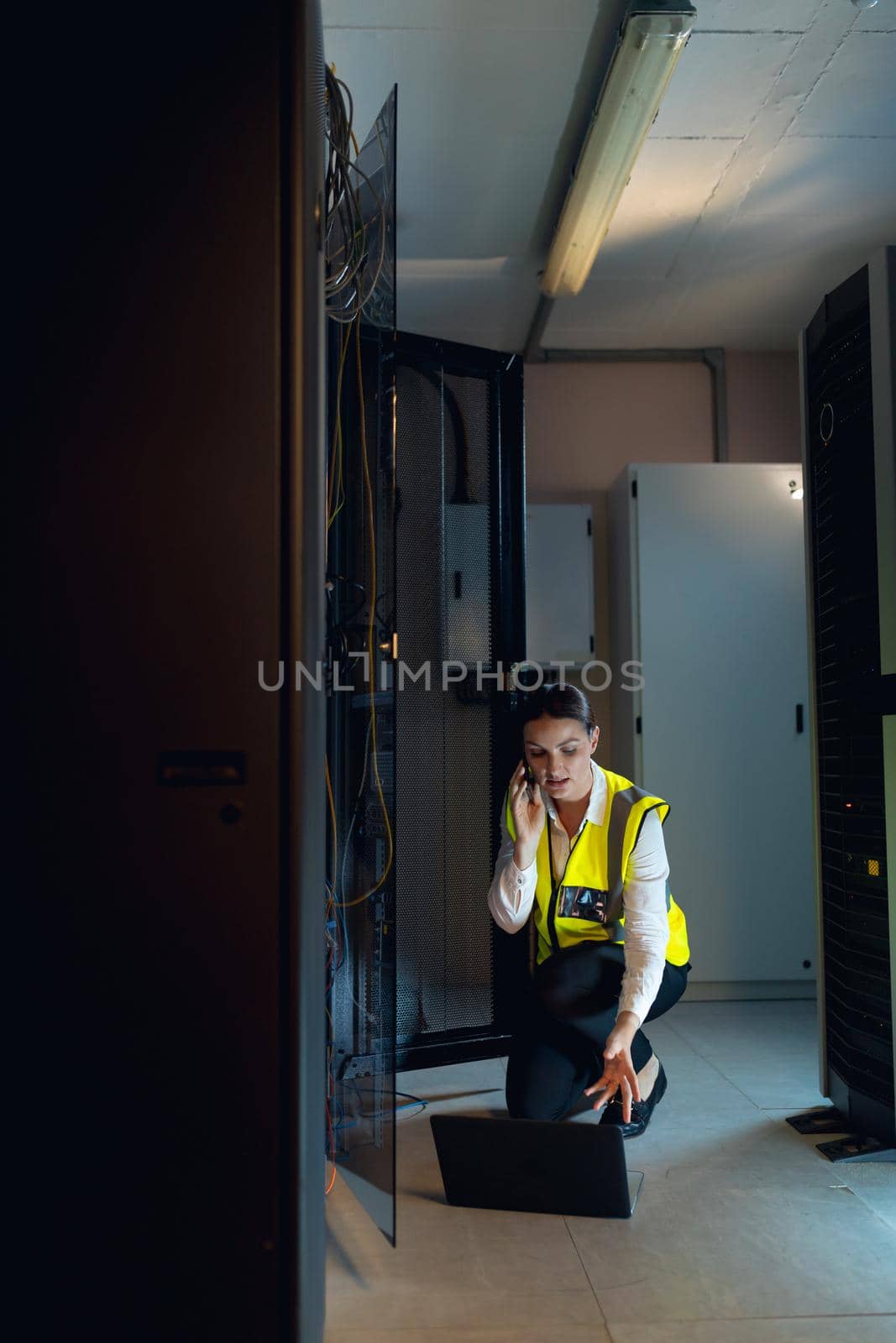 Caucasian female engineer with laptop talking on smartphone while inspecting in computer server room by Wavebreakmedia