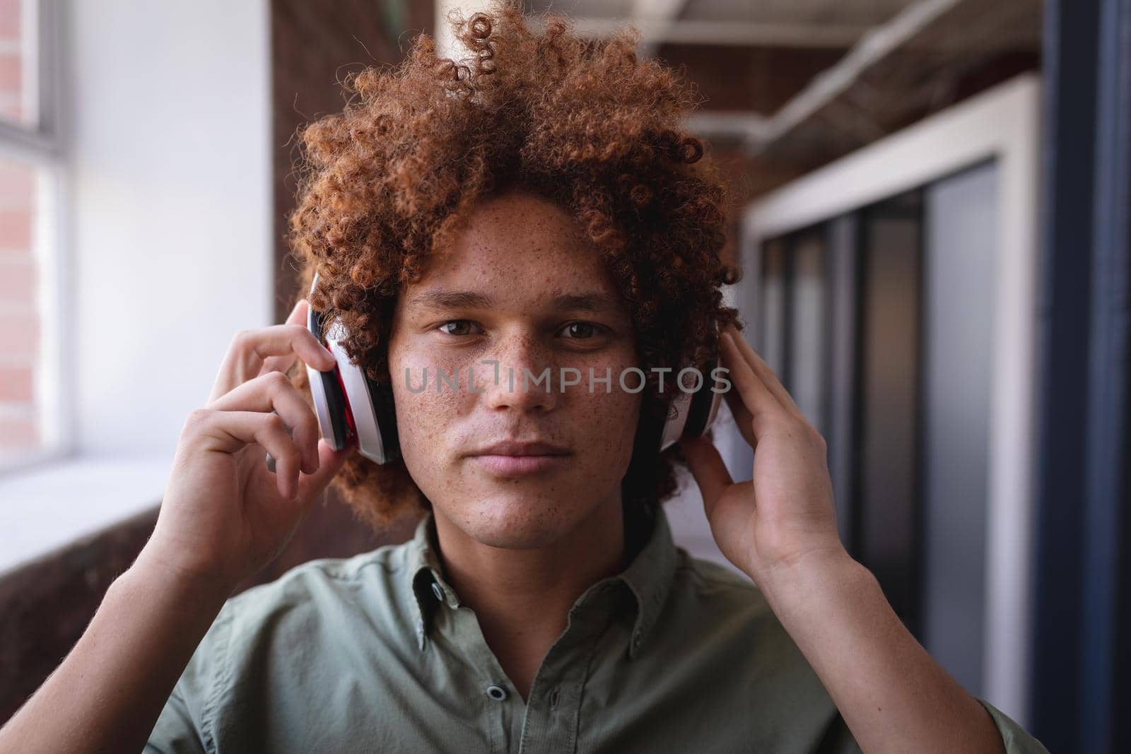 Portrait of happy mixed race businessman standing in office and wearing headphones by Wavebreakmedia