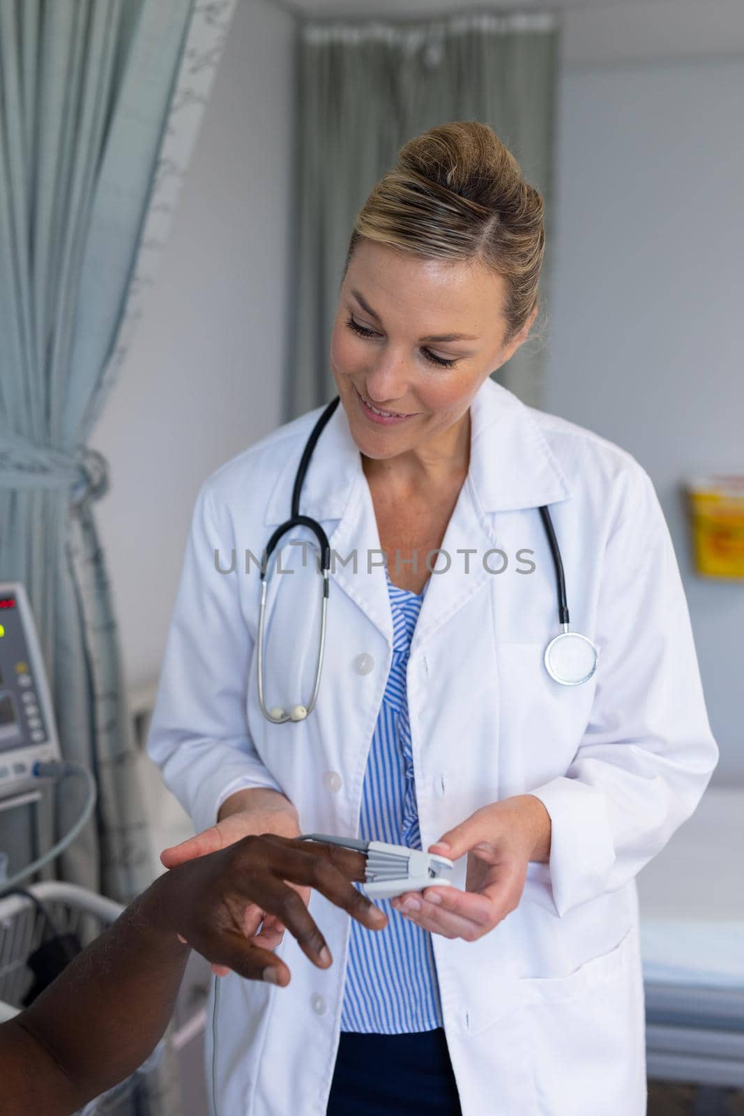 Caucasian female doctor attaching pulse oximeter on male patient finger by Wavebreakmedia