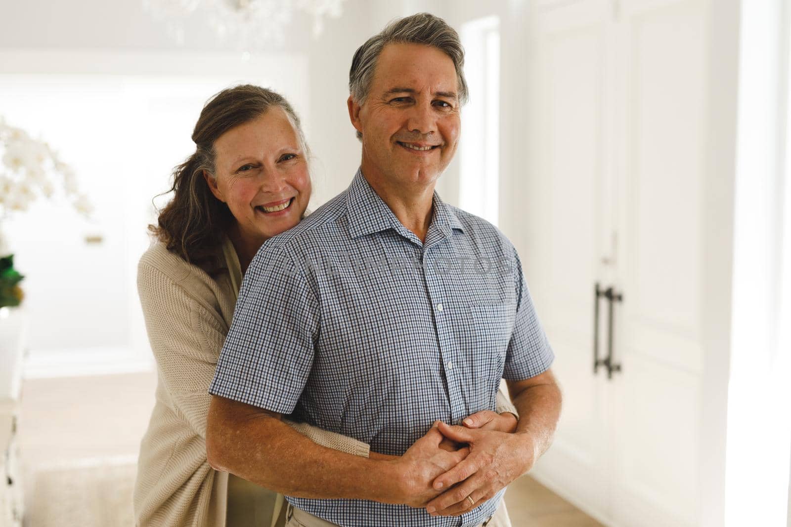 Portrait of happy senior caucasian couple in living room, embracing and smiling. retirement lifestyle, spending time at home.