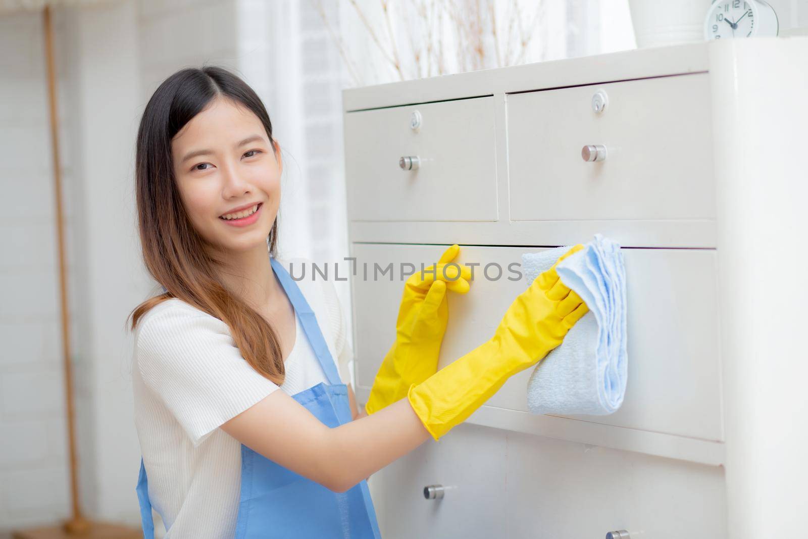 Young asian woman in gloves cleaning home in room, housekeeper is wipe with fabric, housemaid and service, worker polish dust at living room in house, housework and domestic, lifestyle concept.