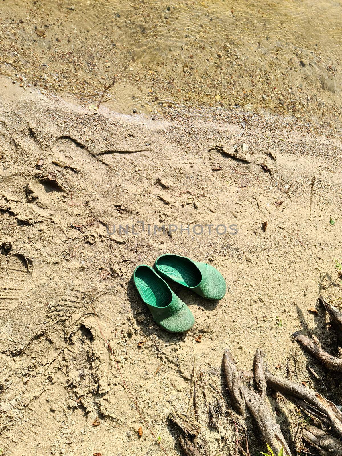 A pair of abandoned flip flops in the sand at a lake
