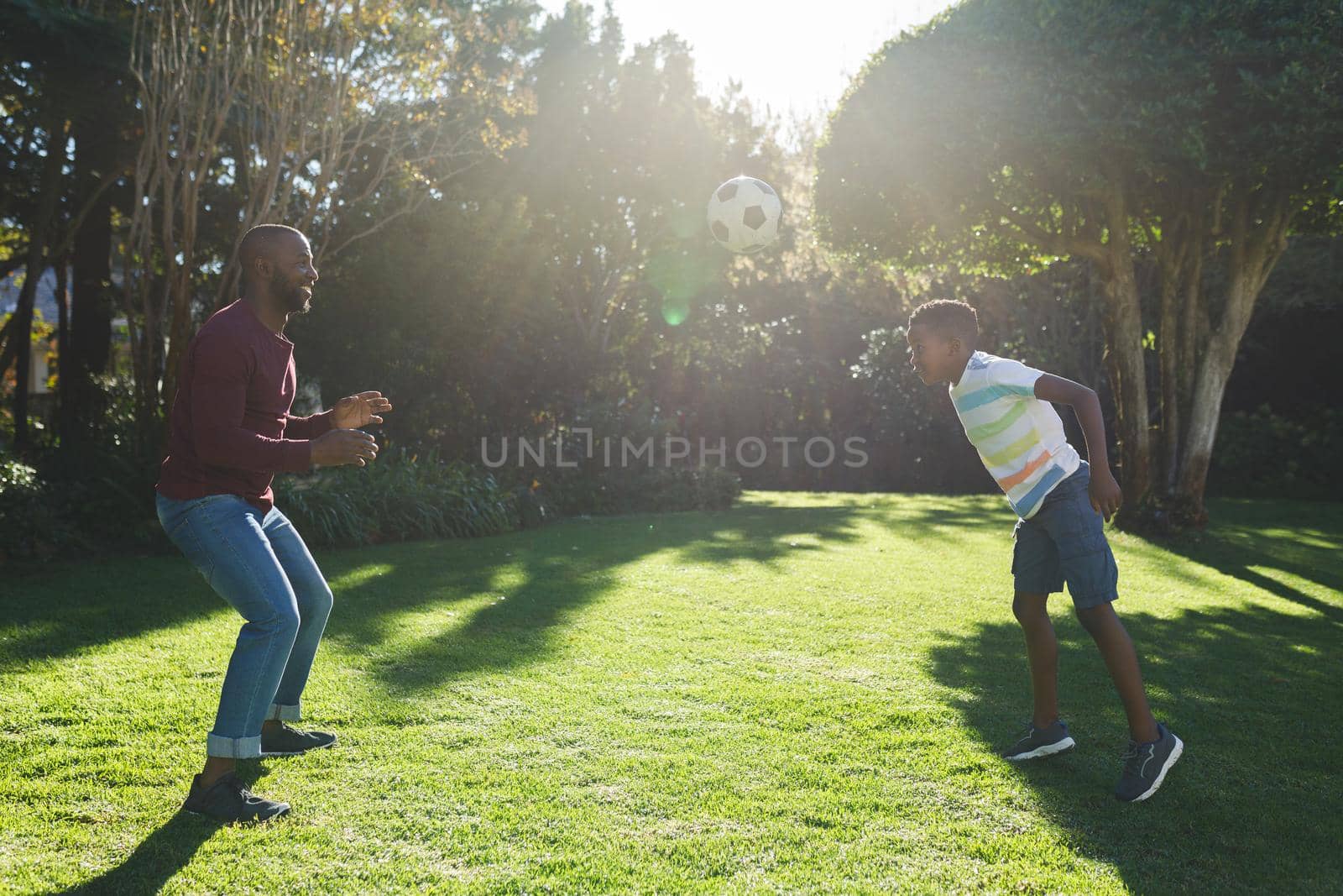 African american father with son having fun and playing football in garden. family spending time at home.