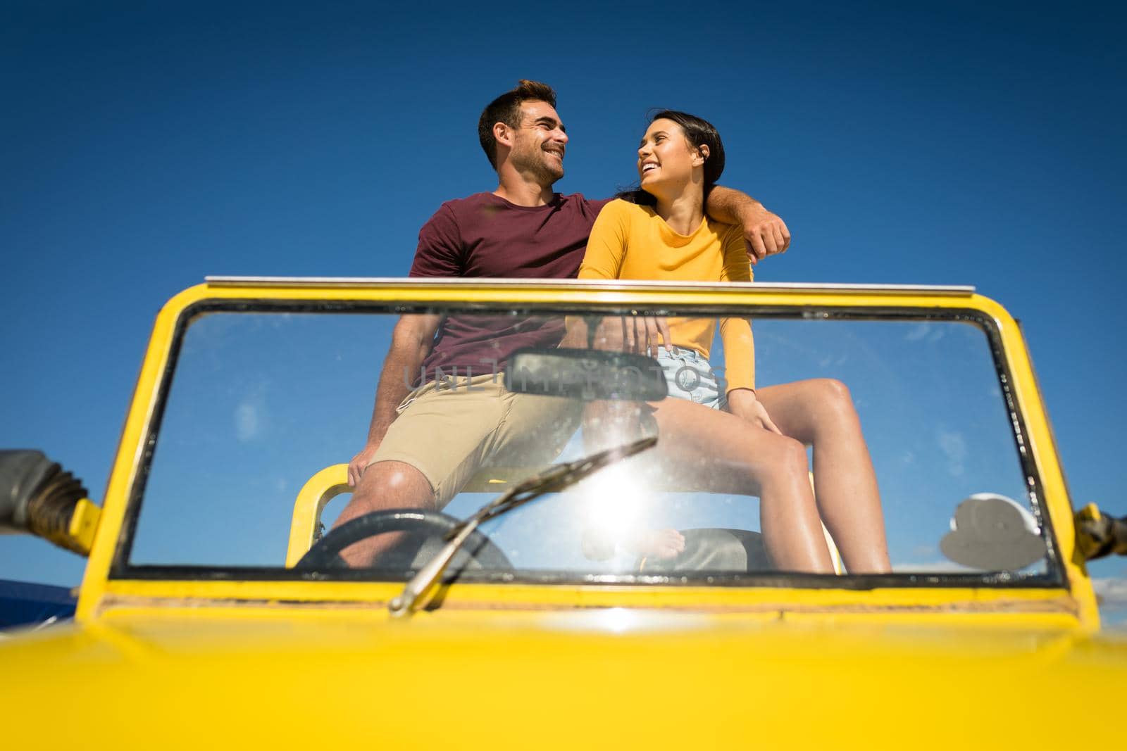 Happy caucasian couple sitting in beach buggy by the sea talking. beach break on summer holiday road trip.