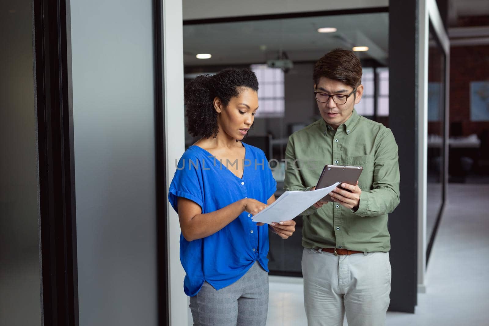 Diverse male and female colleague looking at paperwork and tablet and discussing standing in office. working in business at a modern office.