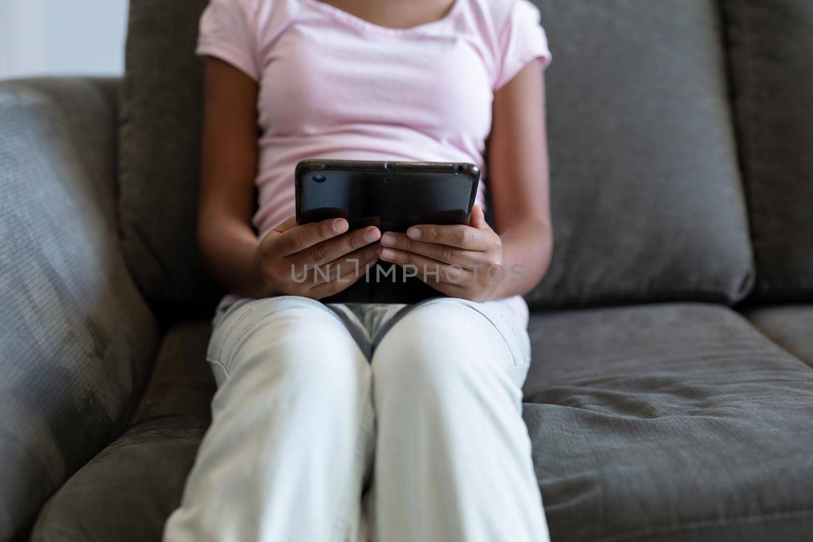 Midsection of mixed race girl sitting on couch using digital tablet by Wavebreakmedia