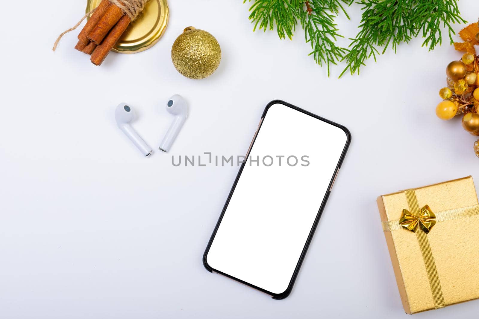 Composition of smartphone with copy space, wireless earphones and christmas decorations on white. christmas, tradition and celebration concept.