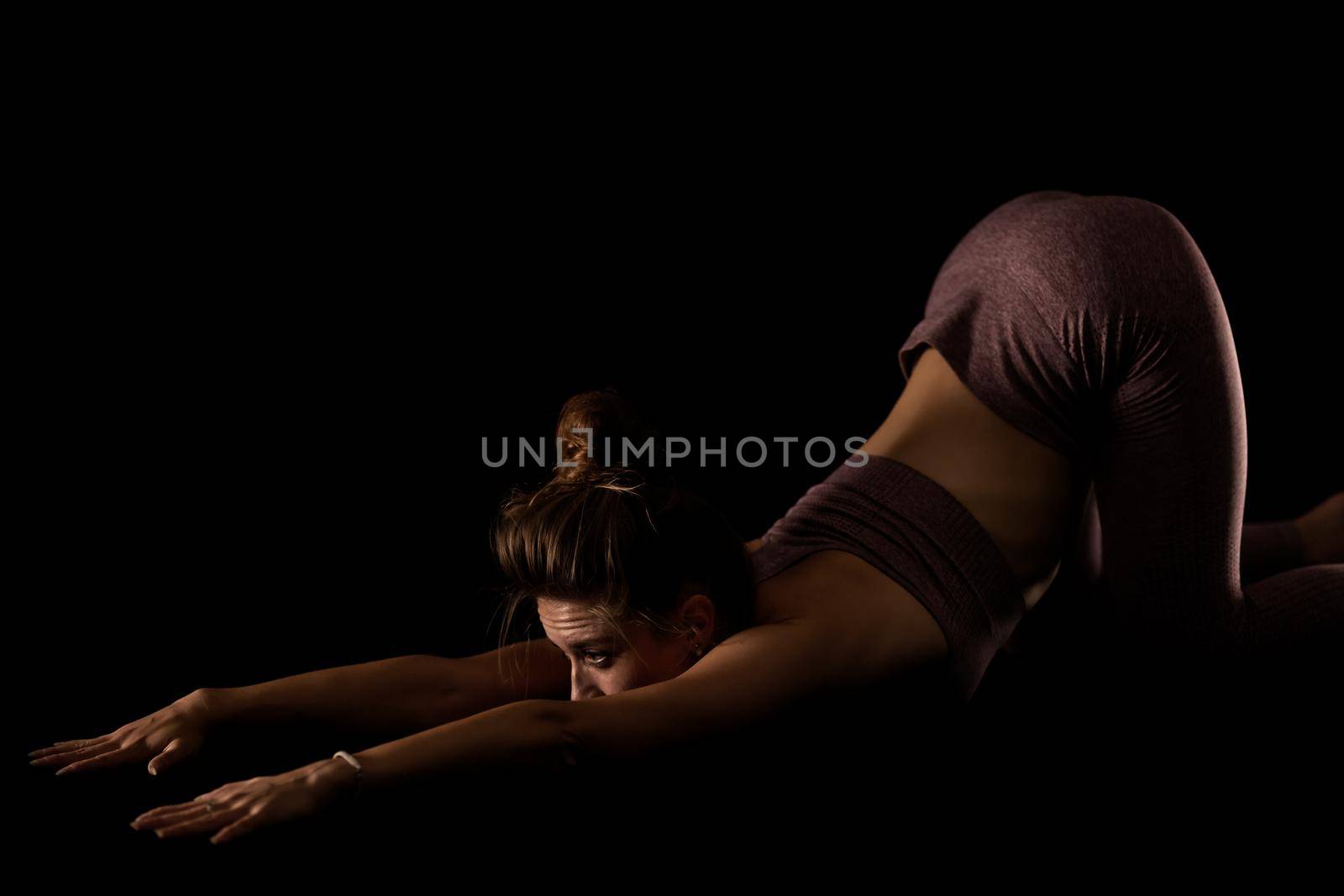 Fit woman practicing yoga poses. Side lit half silhouette girl doing exercise in studio against black background.. by kokimk