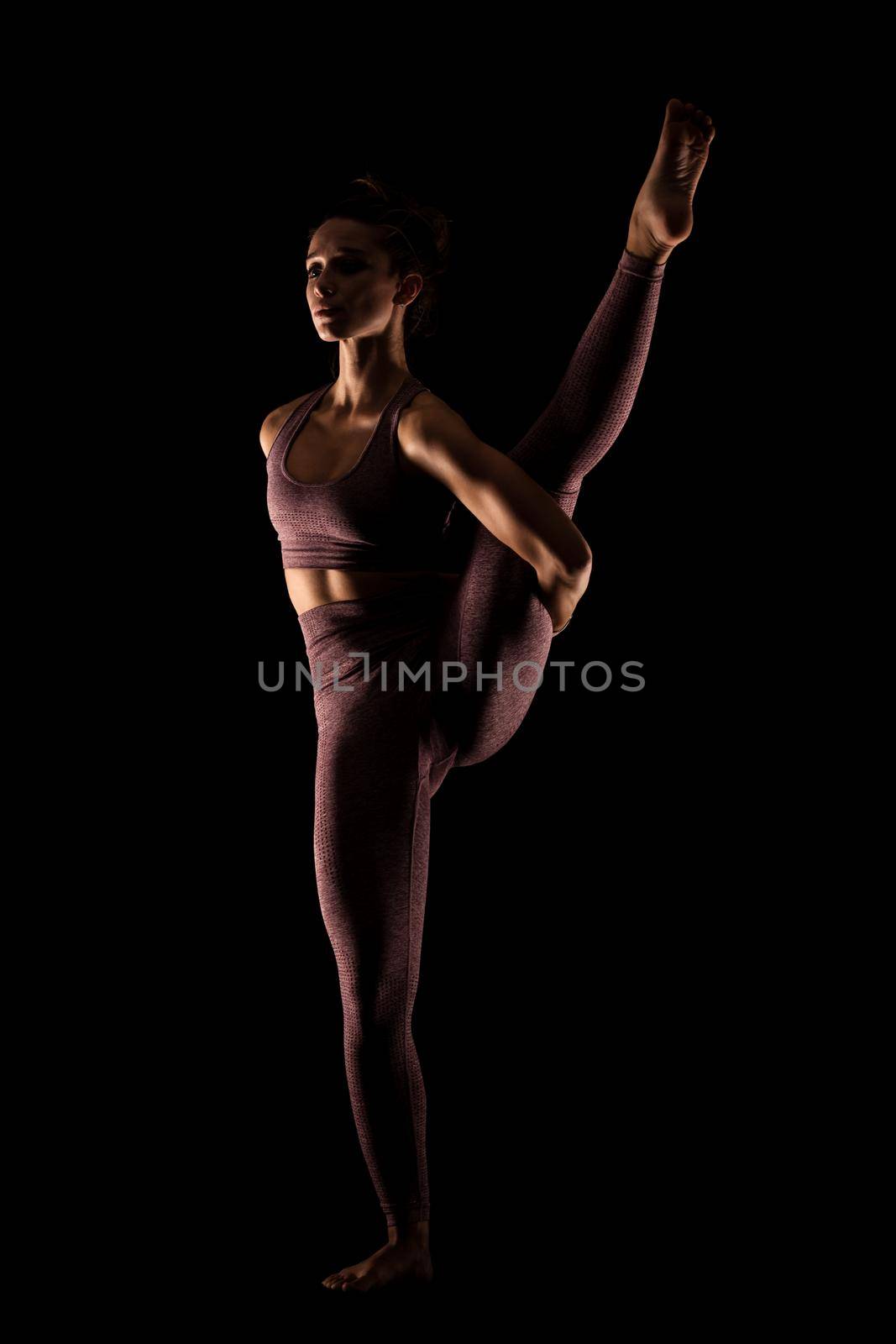 Fit woman practicing yoga poses. Side lit half silhouette girl doing exercise in studio against black background.. by kokimk