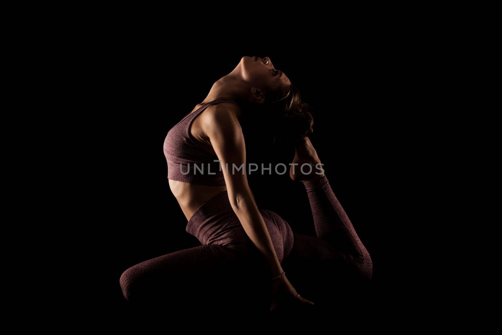 Fit woman practicing yoga poses. Side lit half silhouette girl doing exercise in studio against black background.. by kokimk