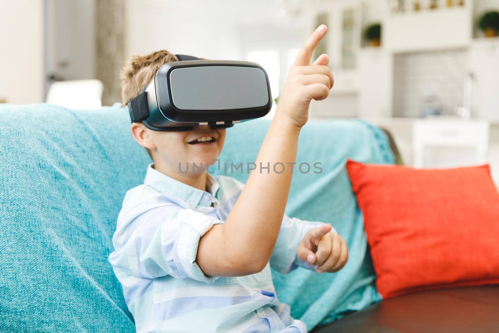 Caucasian boy sitting on couch and using vr headset in living room. childhood leisure time, fun and discovery at at home using technology.