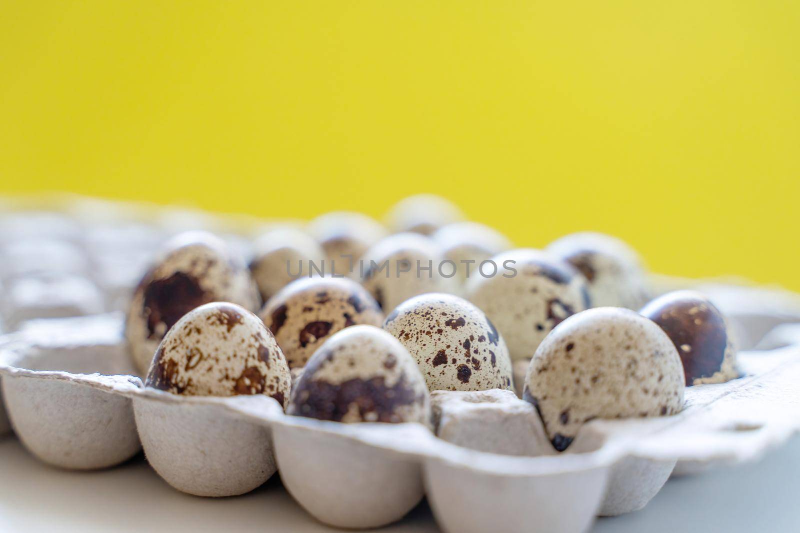 Spotted quail eggs in an egg box on a yellow background, natural eco friendly products. by Matiunina