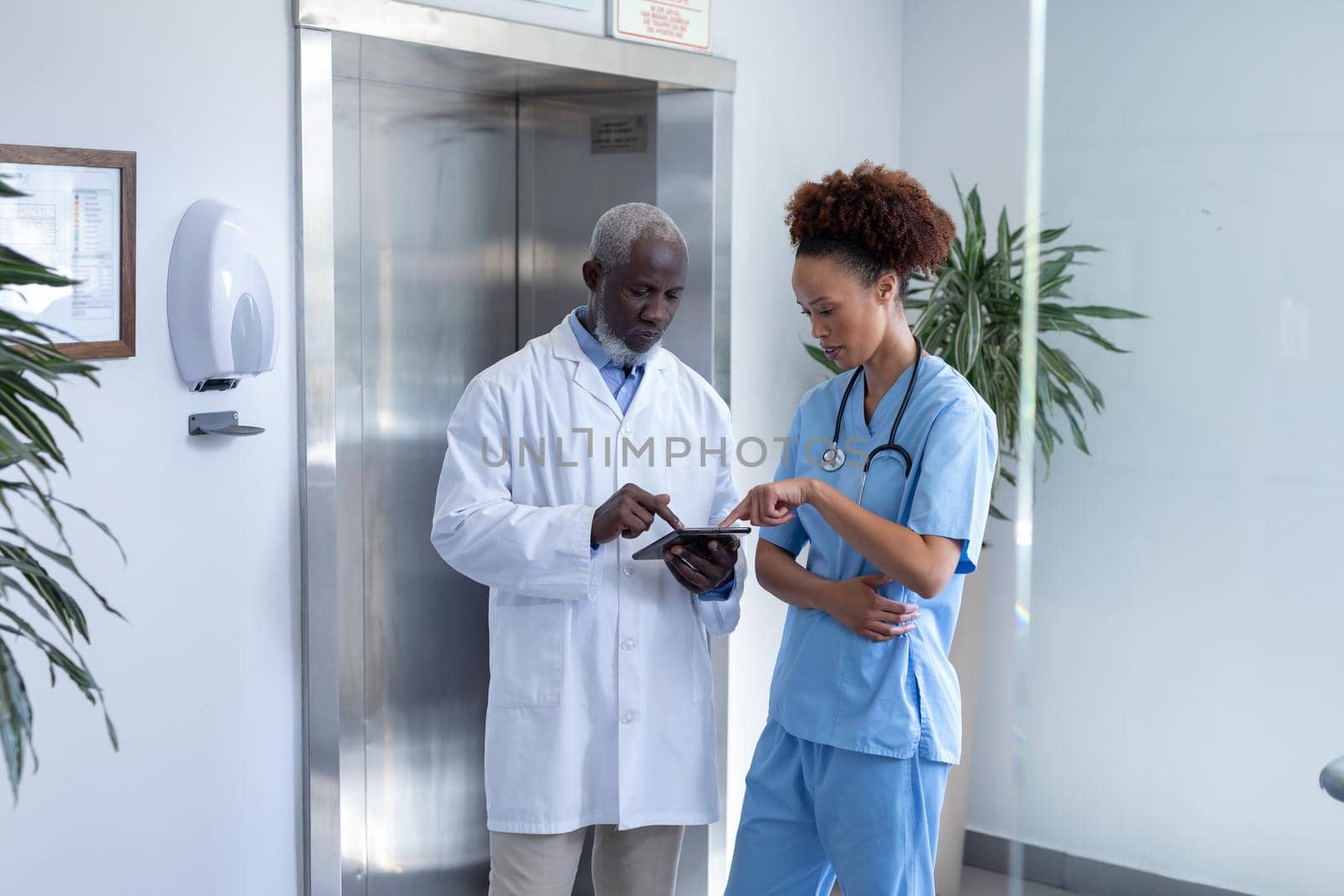 Diverse male and female doctors using tablet and discussing in hospital corridor by Wavebreakmedia