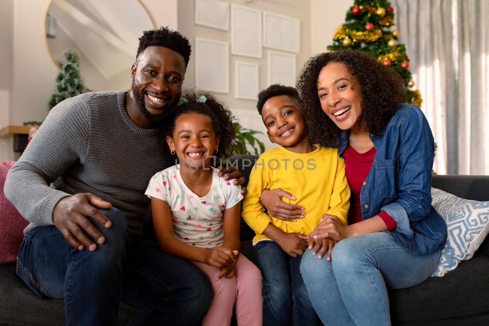 Happy african american family sitting on sofa and looking at camera. family christmas time and festivity together at home.