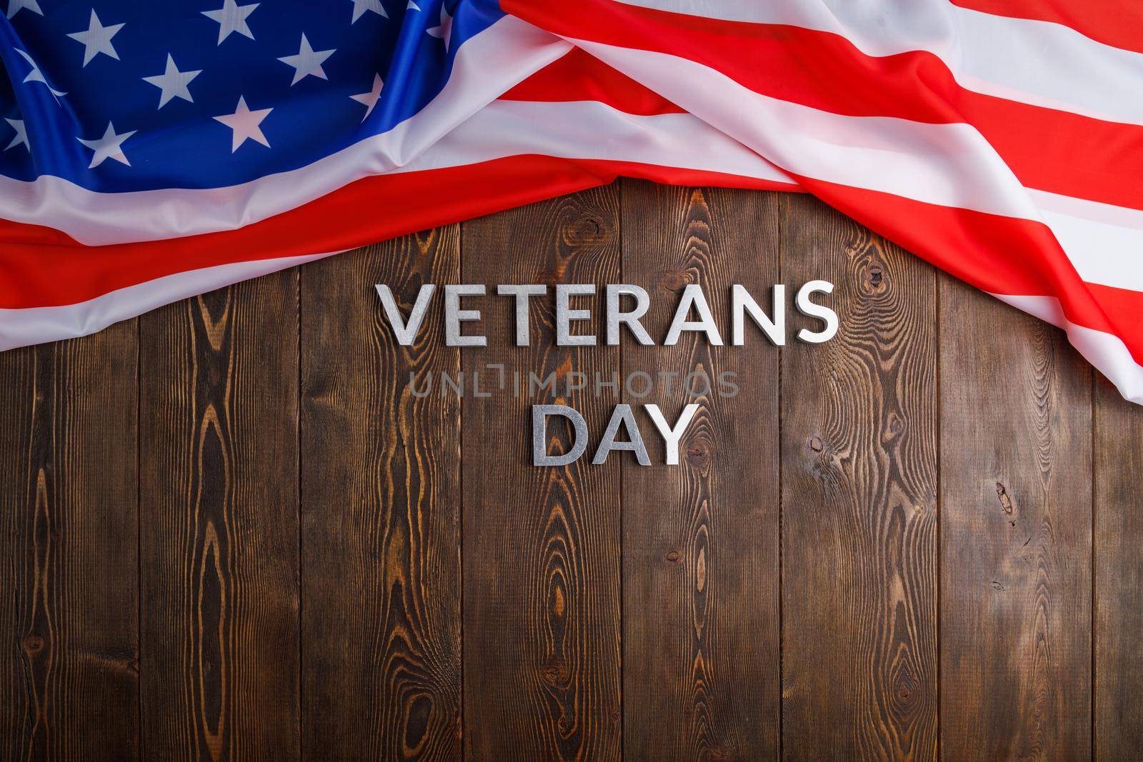 the words veterans day laid with silver metal letters on wooden board surface with crumpled usa flag on upper side, high angle flat lay perspective