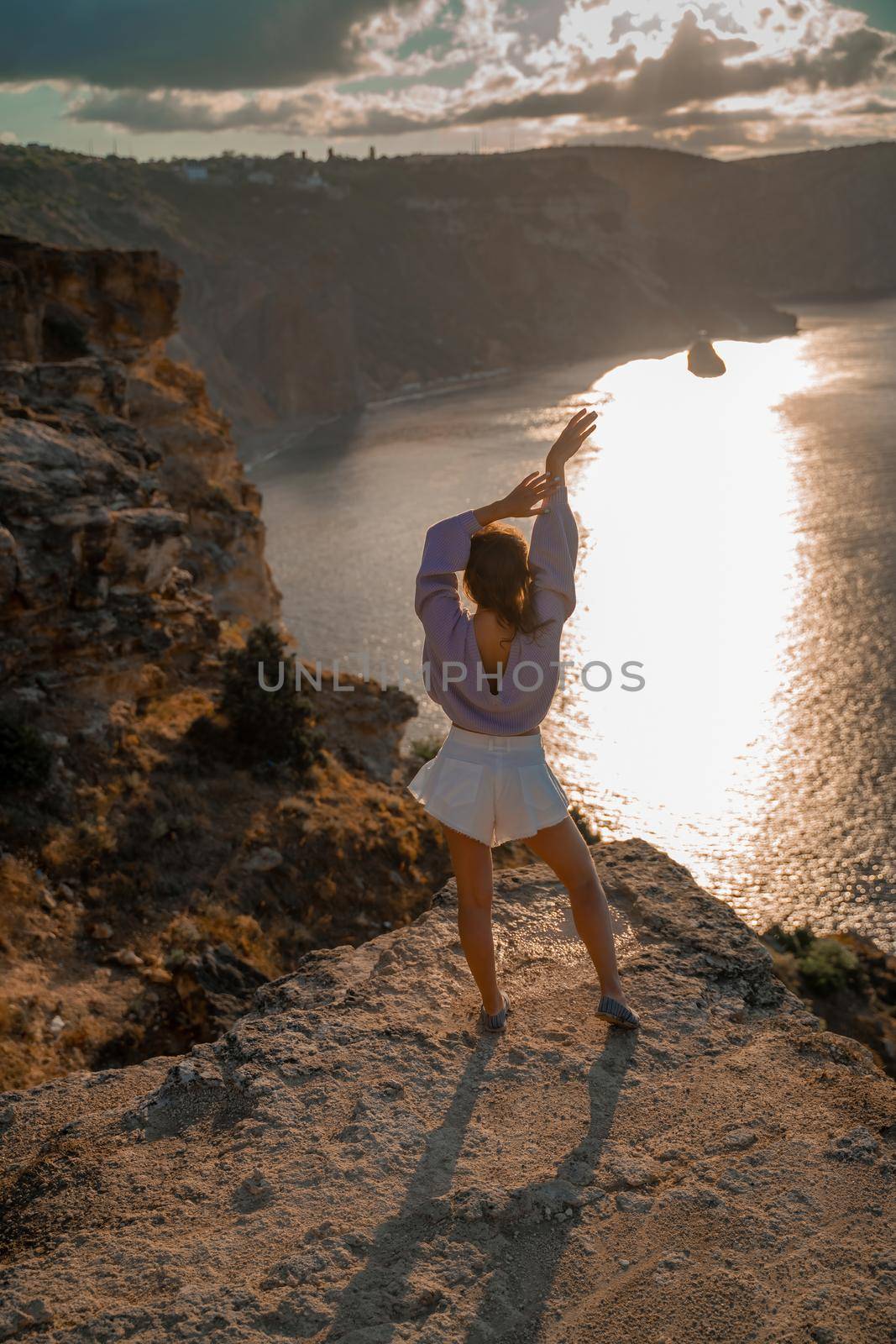 Free girl with open arms at sunset over the sea, sun over clouds, sunset in the mountains, golden hour, silhouette of a woman at sunset on the mountain by Matiunina