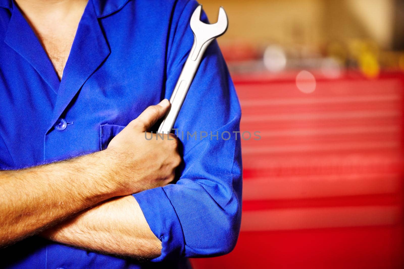 Cropped image of a male mechanic holding a spanner with his arms folded.