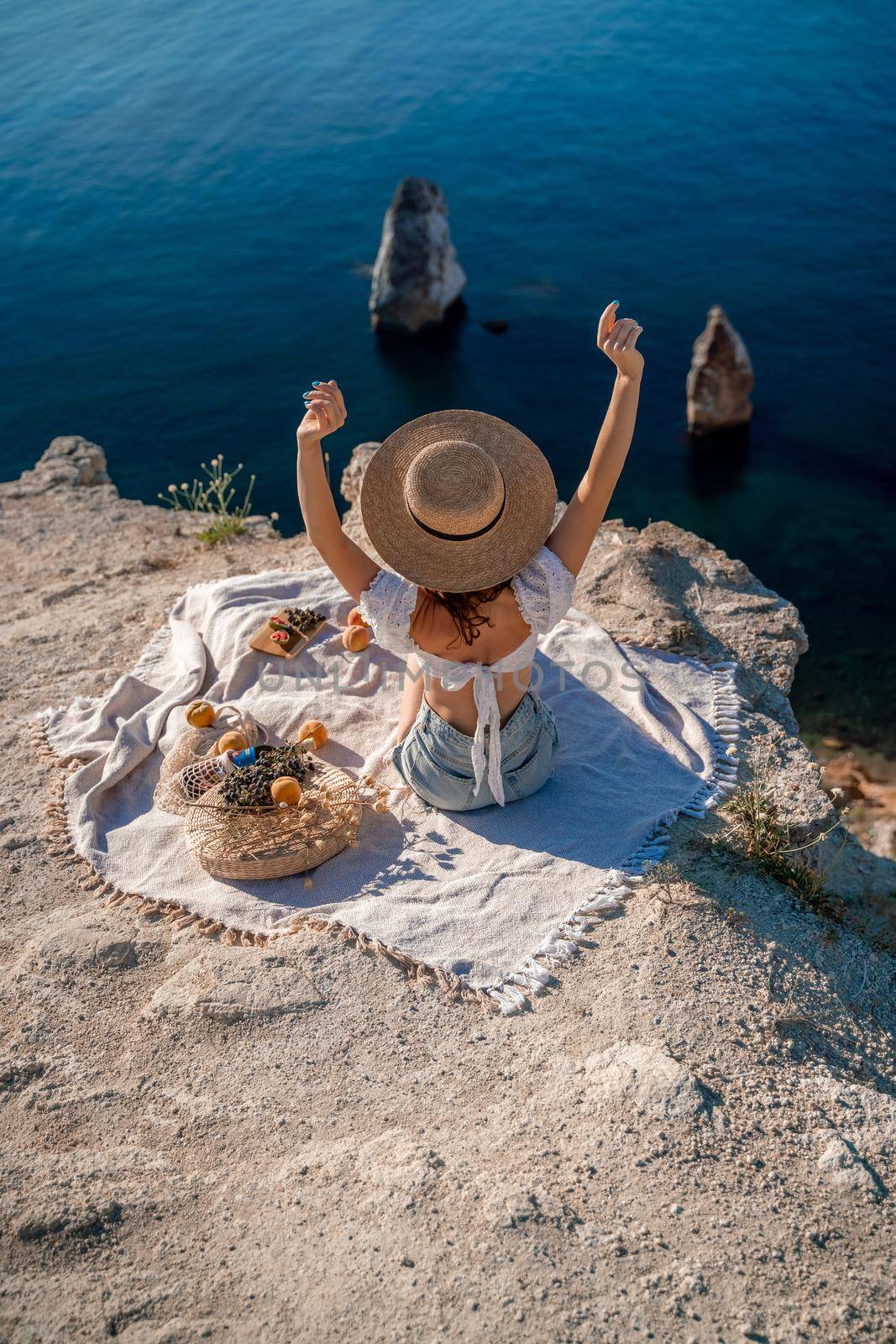 Street photo of a beautiful woman with dark hair in a white top, shorts and a hat having a picnic on a hill overlooking the sea by Matiunina