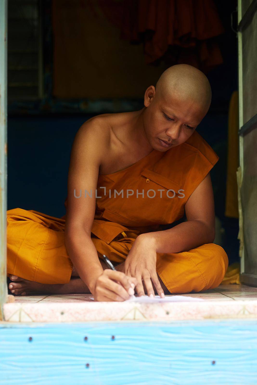 Shot of a buddhist monk filling in a form while sitting in the doorway of his home.