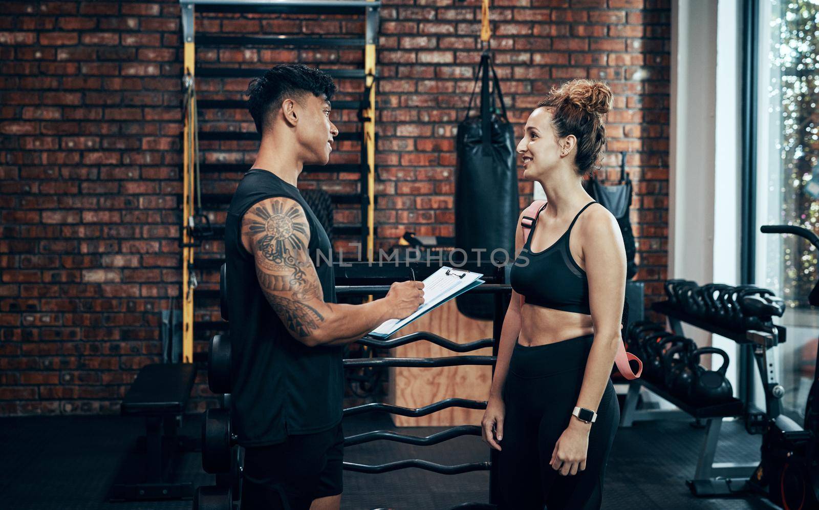 Signup with us, you wont regret it. Shot of a sporty young woman talking to a fitness trainer at the gym. by YuriArcurs