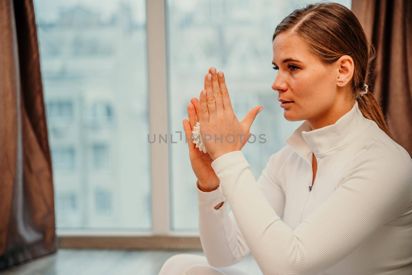 Athletic slim caucasian woman doing thigh self-massage with a massage ball indoors. Self-isolating massage.