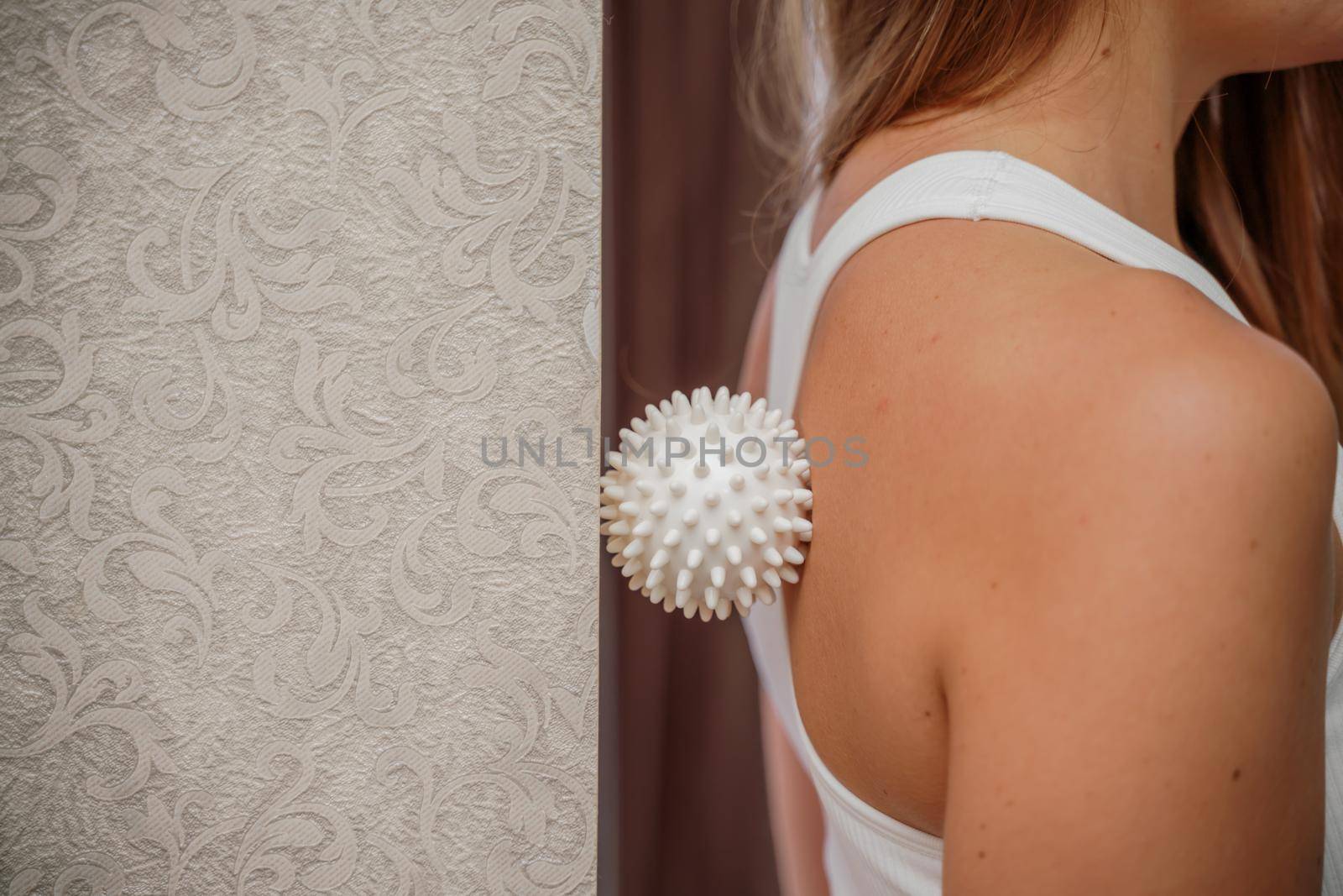 Athletic slim caucasian woman doing thigh self-massage with a massage ball indoors. Self-isolating massage.