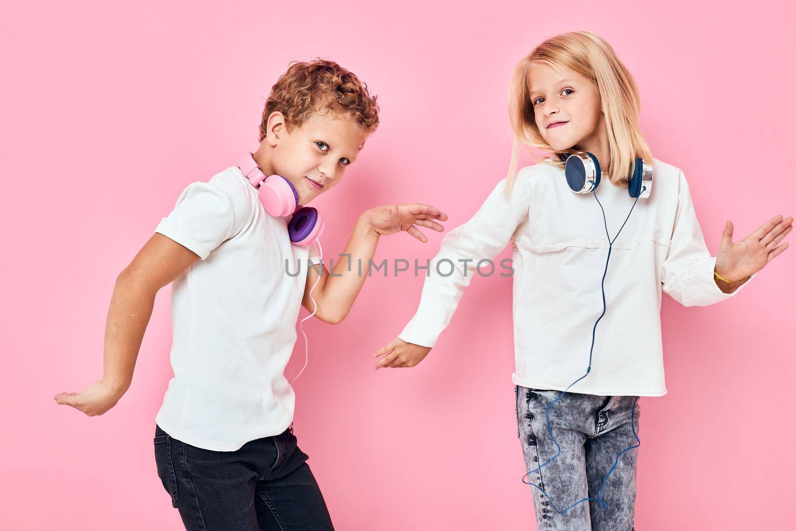 Stylish little boy and cute girl listening to music pink color background. High quality photo