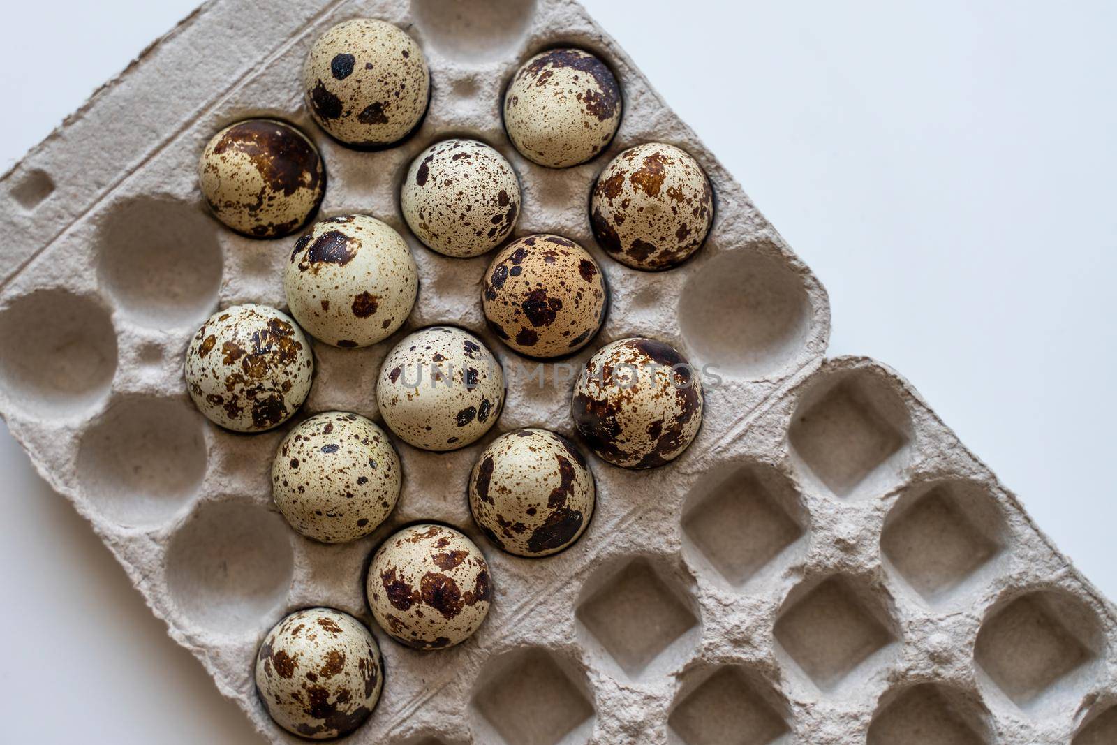 Spotted quail eggs in an egg box on a light background, natural eco-friendly products. by Matiunina