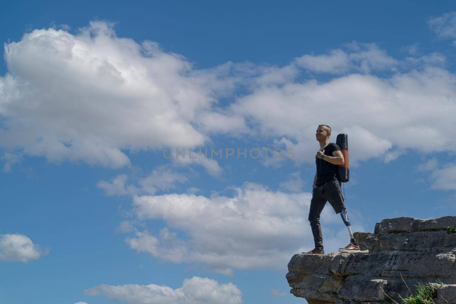 a man on a prosthetic leg travels the mountains. Dressed in black jeans and a T-shirt, he carrying mat.