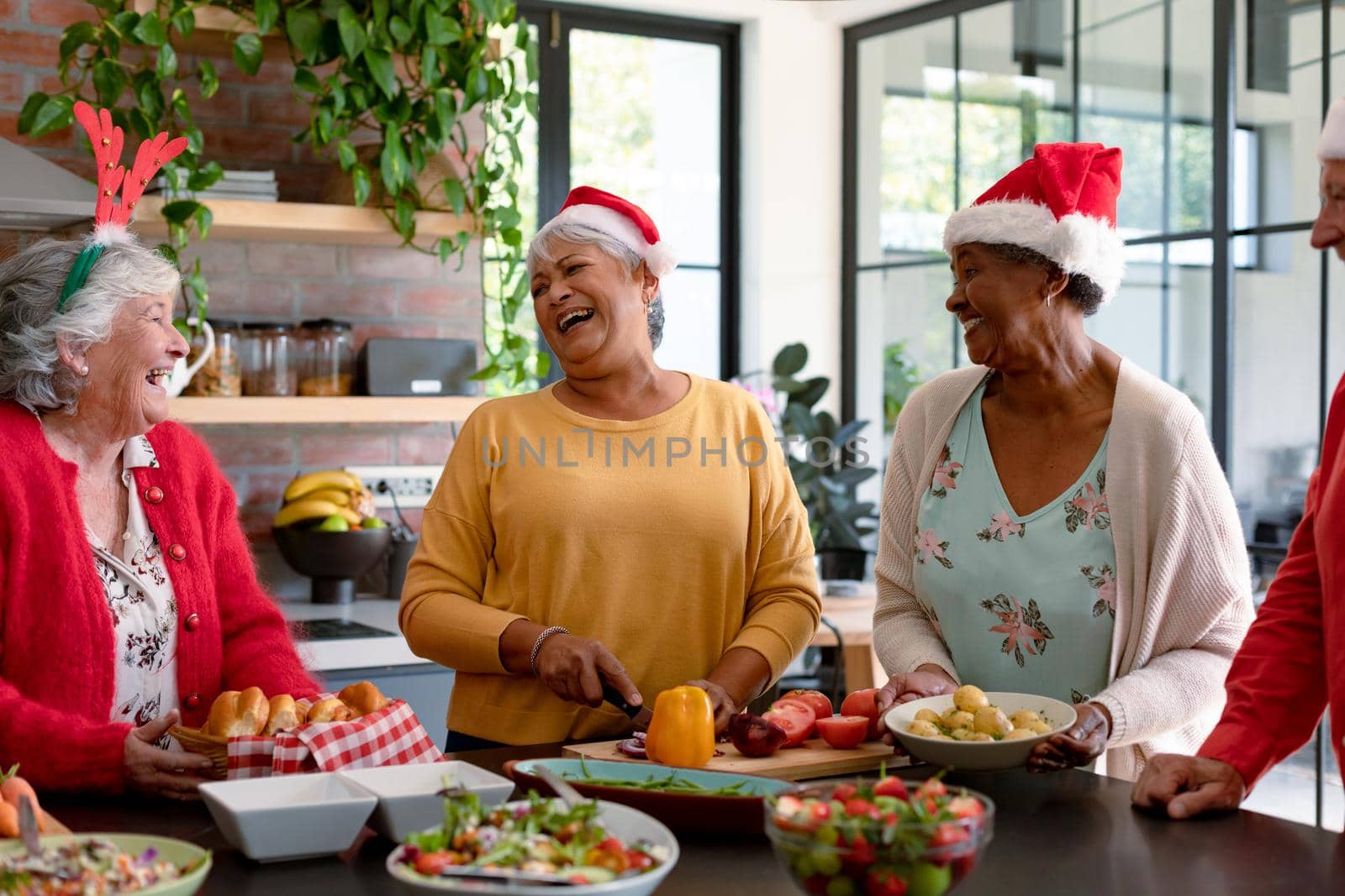Four happy diverse senior male and female friends in christmas hats cooking together in kitchen by Wavebreakmedia