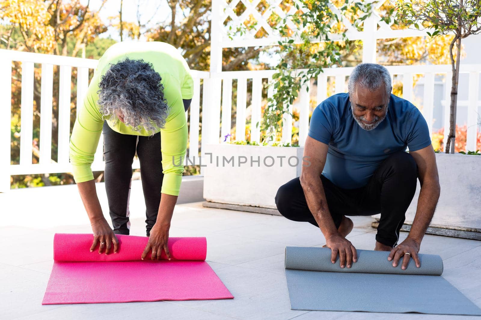Smiling african american senior couple rolling yoga mats in garden by Wavebreakmedia