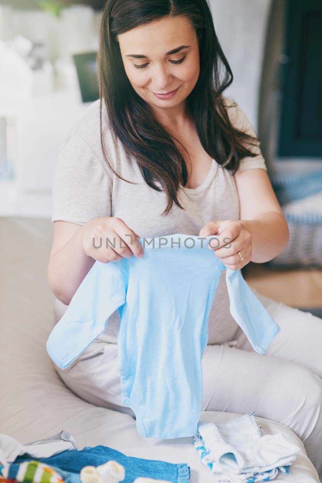 I cant wait to play dress up. Cropped shot of a pregnant woman sorting baby clothes. by YuriArcurs