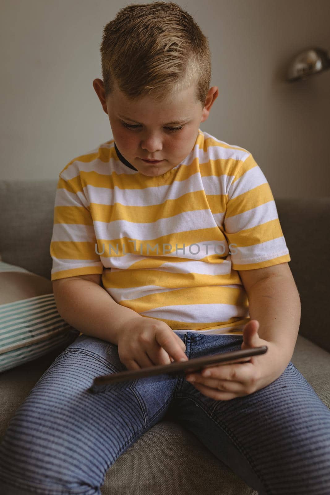 Caucasian boy using digital tablet sitting on the couch at home. childhood, technology and home concept
