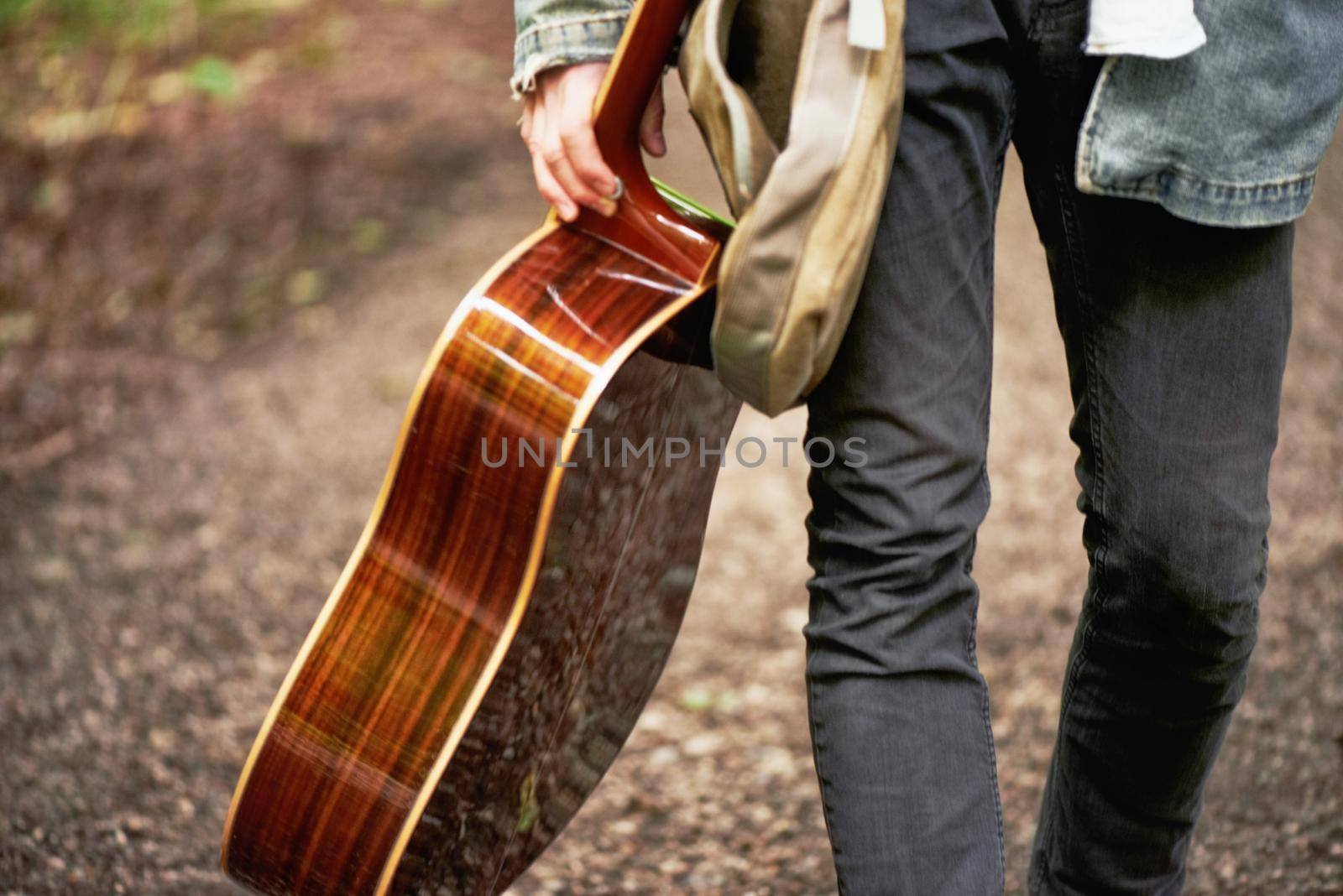 Modern traveling minstrel. A cropped closeup shot of a young man carrying a guitar while walking down a forest path. by YuriArcurs
