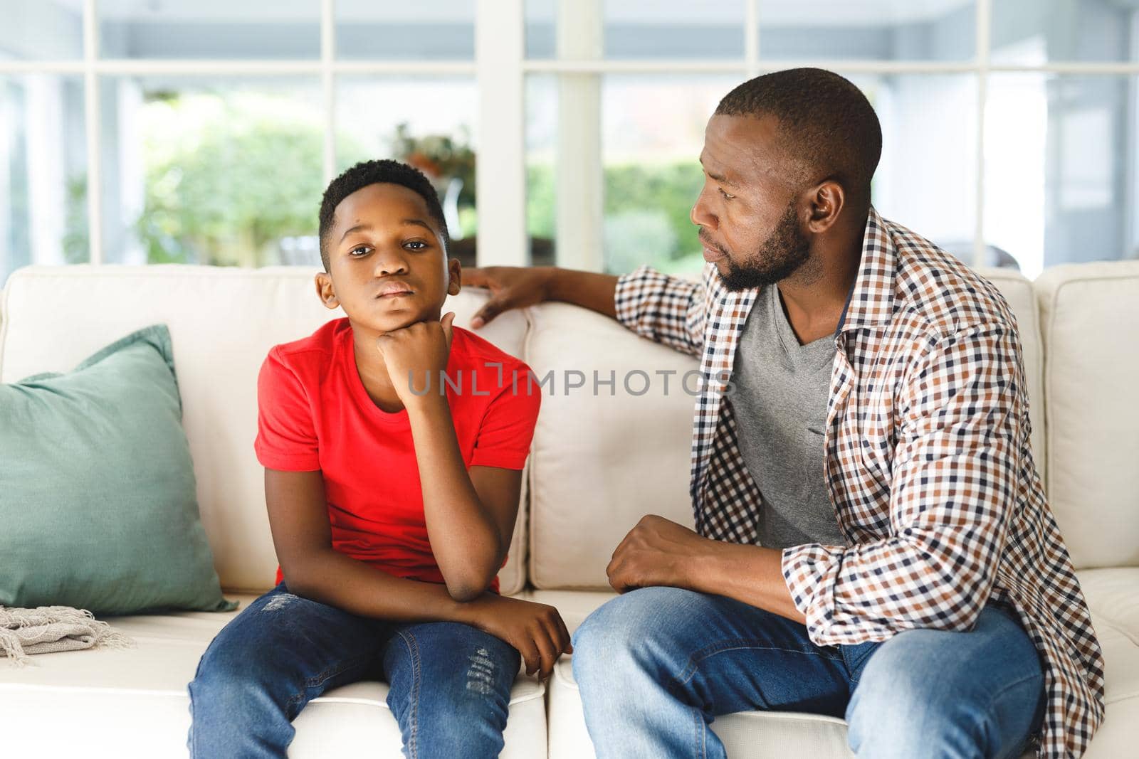 African american father sitting on couch talking to son in living room. family spending time at home, father son relationship.