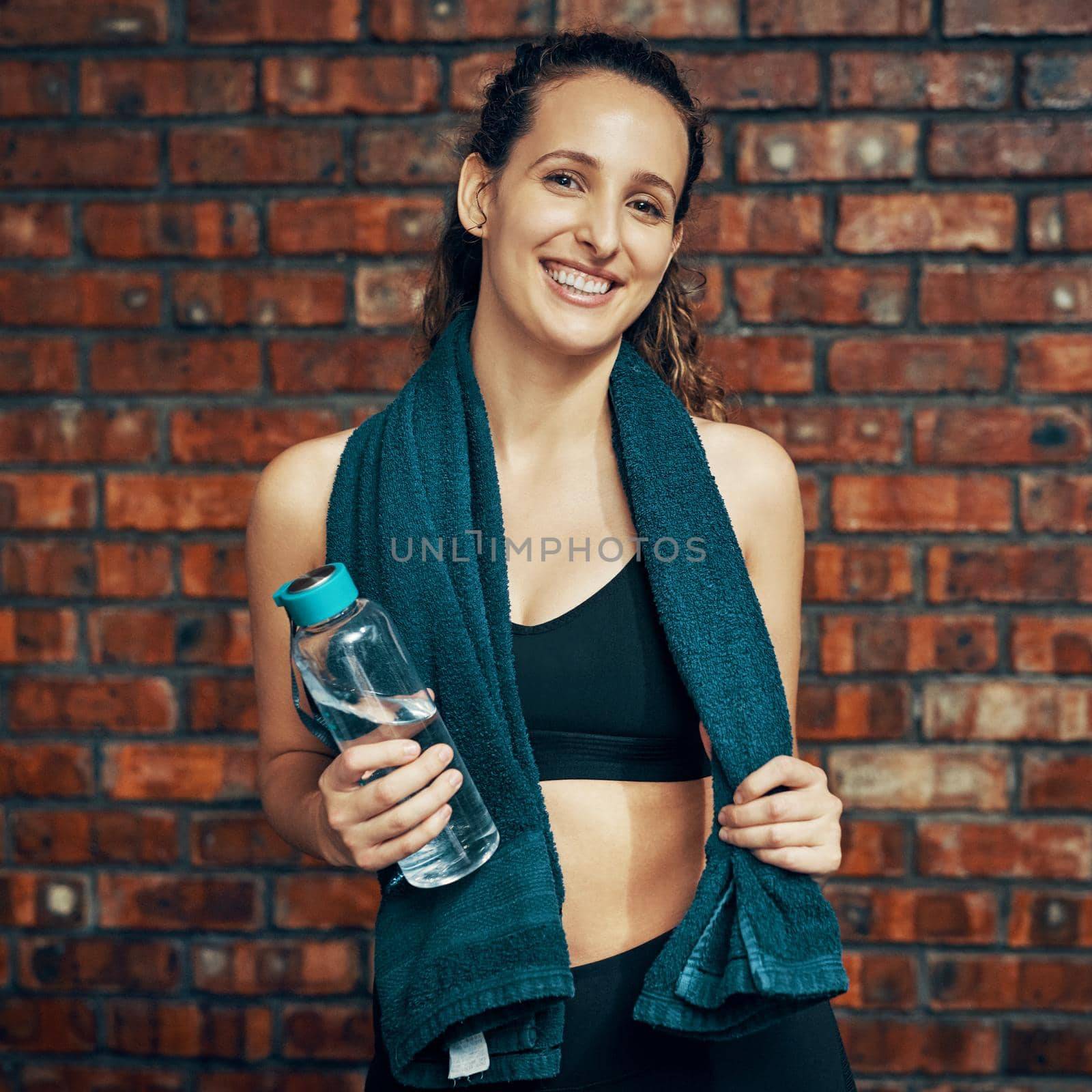 Cropped shot of a young woman posing with a water bottle and her towel at the gym.