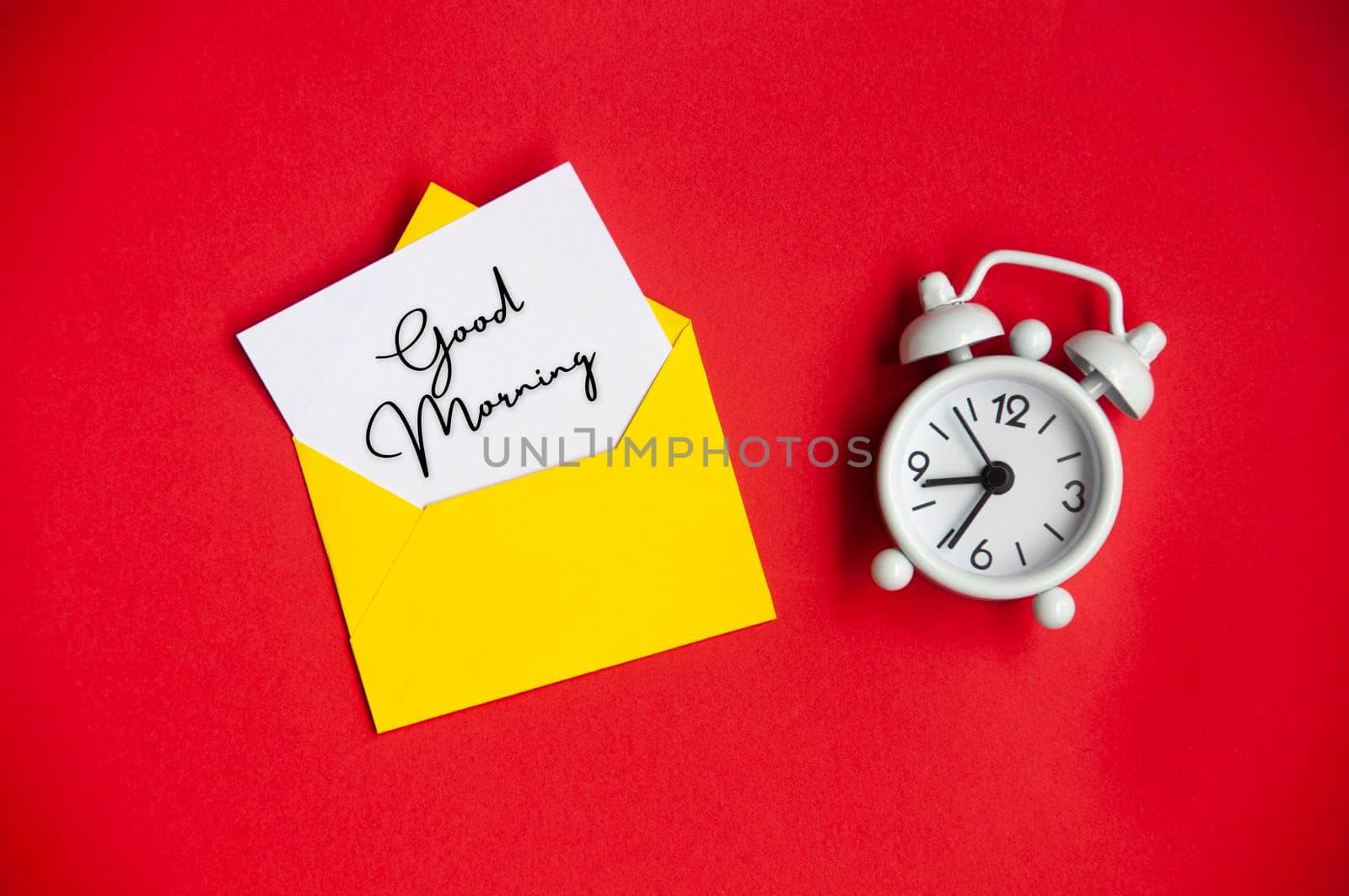 Good morning text on white notepad with envelope and alarm clock background. Morning concept