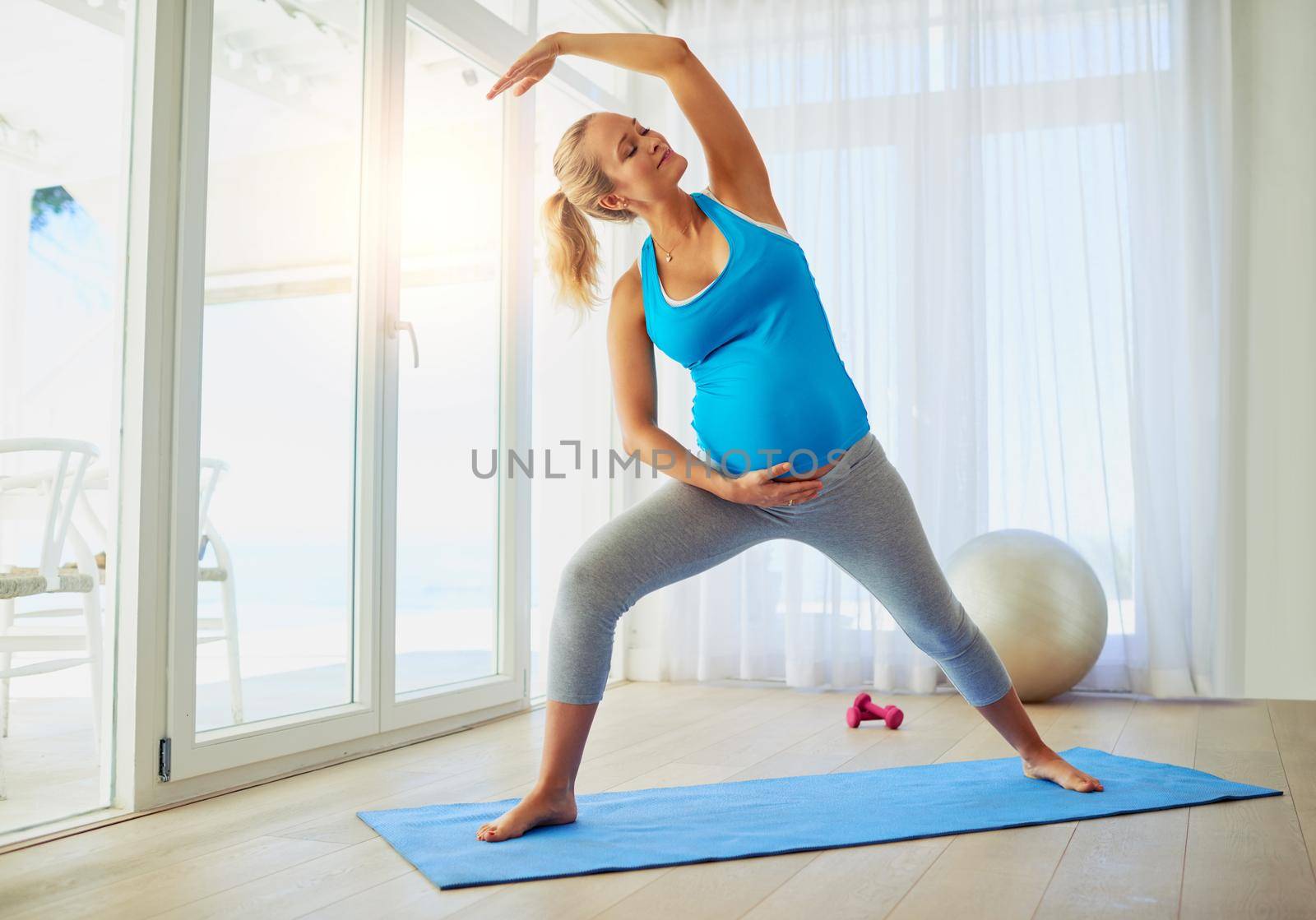 Reaching for her pregnancy fitness goals. Shot of a pregnant woman working out on an exercise mat at home. by YuriArcurs
