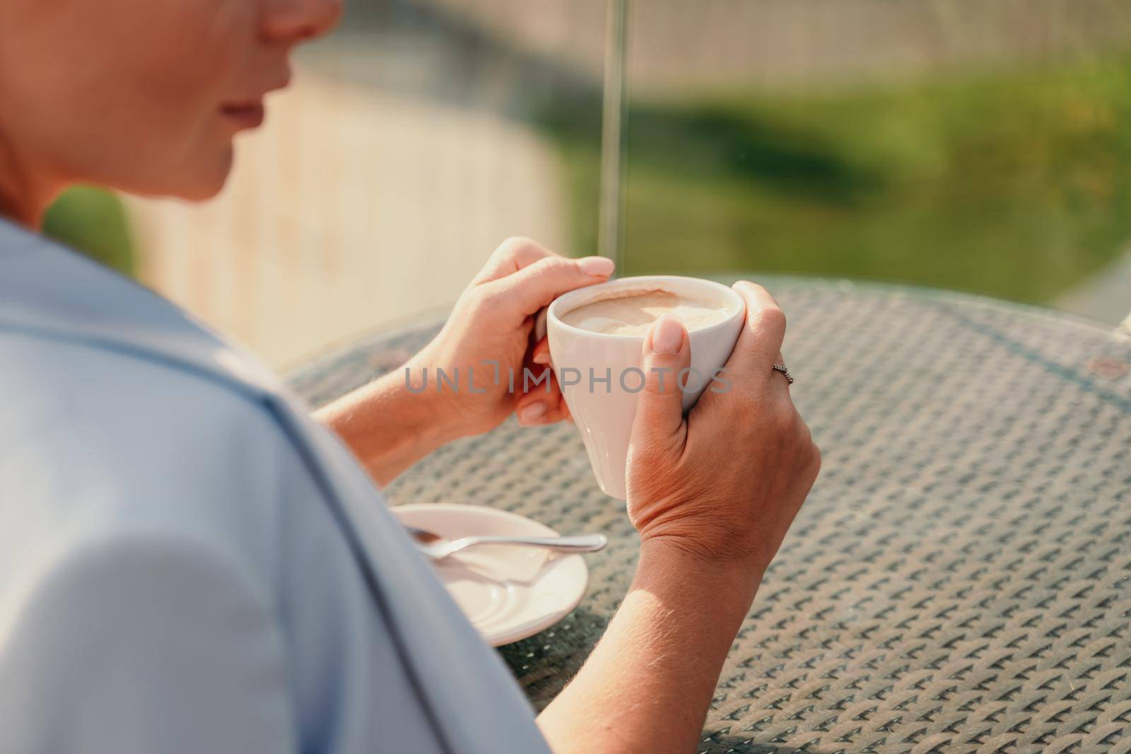 A middle-aged woman sits in a street cafe overlooking the mountains at sunset. She is dressed in a blue jacket and drinks coffee admiring the nature. Travel and vacation concept