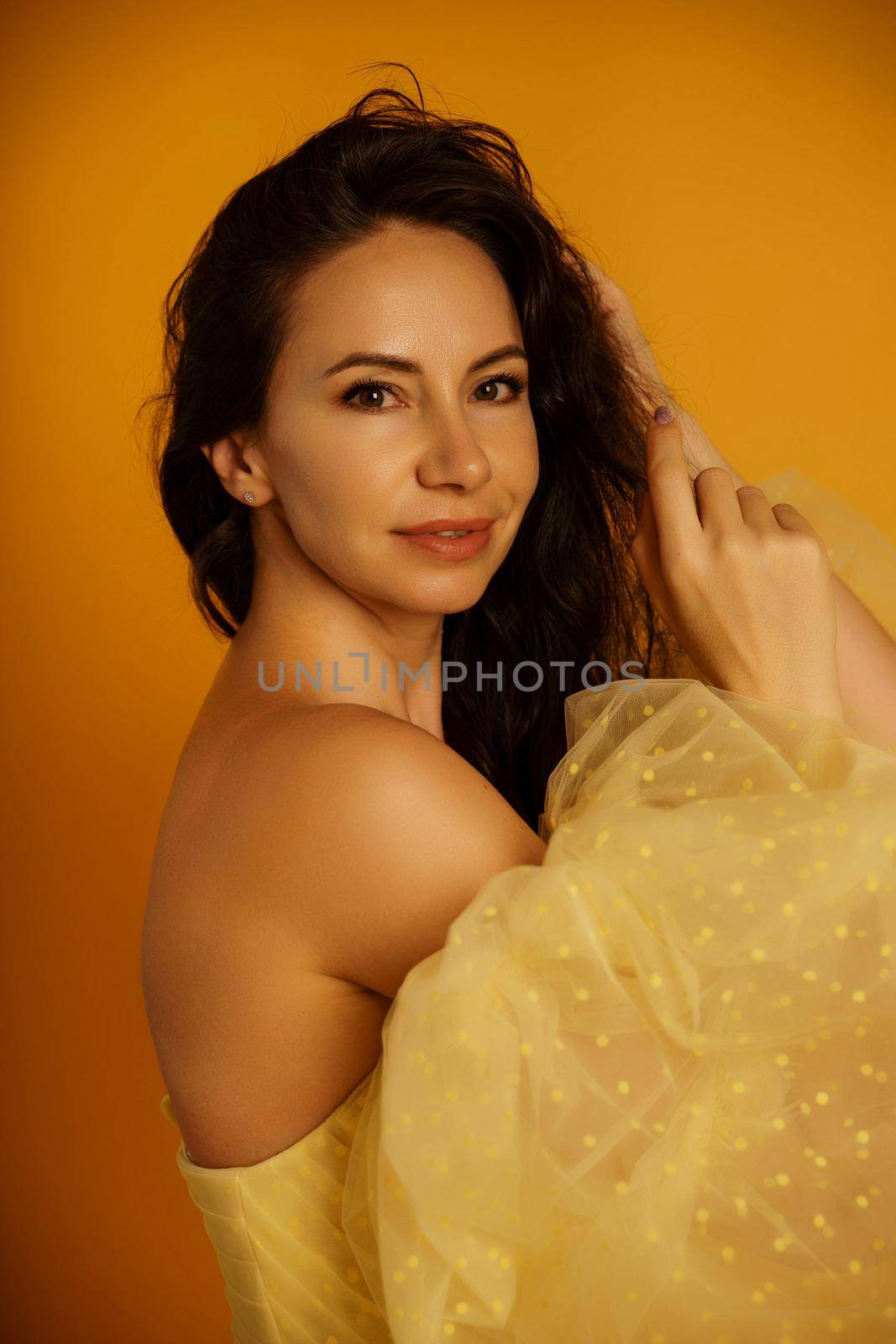 Profile portrait of a beautiful middle-aged woman in a yellow dress, her hair pulled up against a yellow background.