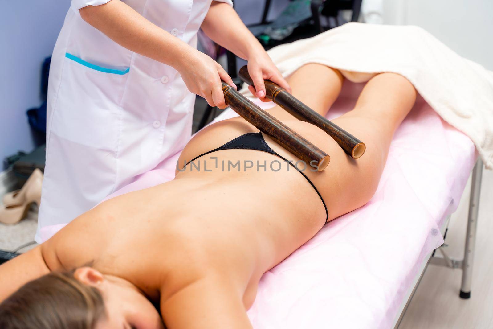Woman having massage with bamboo stick in wellness center