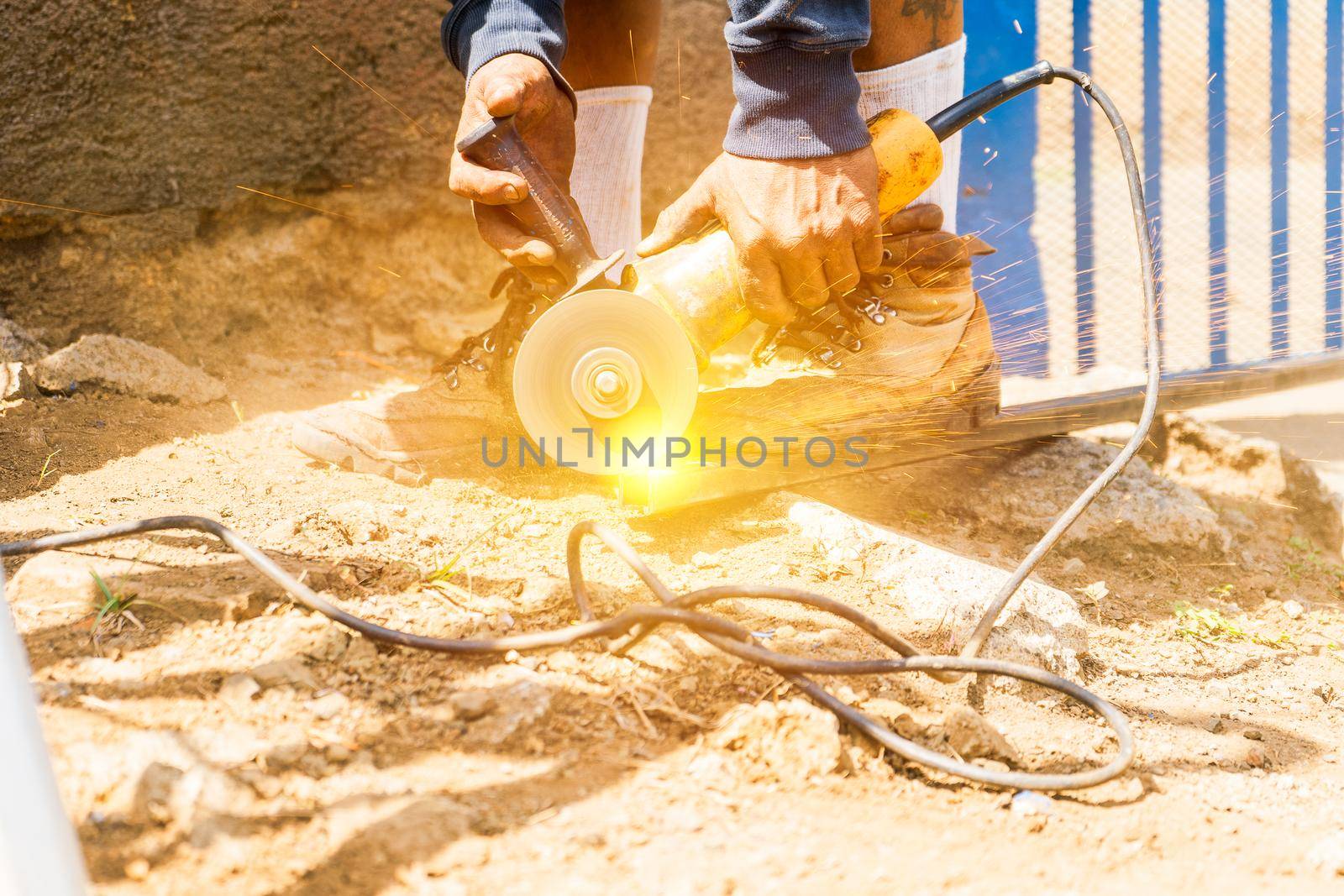 Closeup of the hands of a latin blue collar worker using a handheld circular saw to cut a tube in the dirt floor