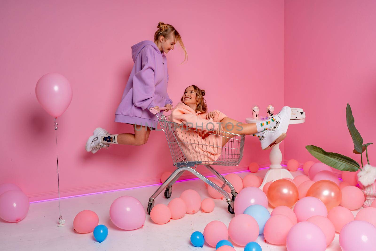 Two beautiful attractive funny joyful cheerful relaxed carefree girls dressed in casual fashion clothes isolated on hot pink background.